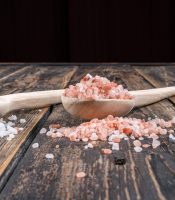Himalayan salt in a wooden spoon and nearby side view on a dark wooden background vertical Himalayan salt in a wooden spoon and nearby side view on a dark wooden background vertical