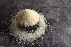 Milled rice in a black bowl on the black cement floor. Selective focus